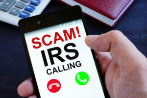 IRS telephone scams showing hand holding phone with scams alert - Stableford Blog