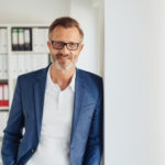 financial planning strategies for the self-employed business man smiling with glasses and office in background