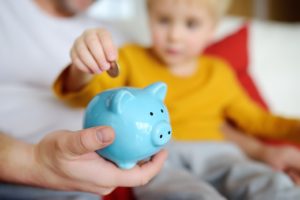 Psychology of Investing Father and Son putting money in piggy bank-web