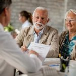 signing up for medicare at age 65 - older couple talking about documents - web