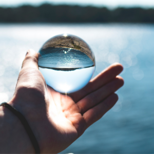 Man holding a glass ball over a lake with mountains in the background - the reflection in the glass ball is upside down.